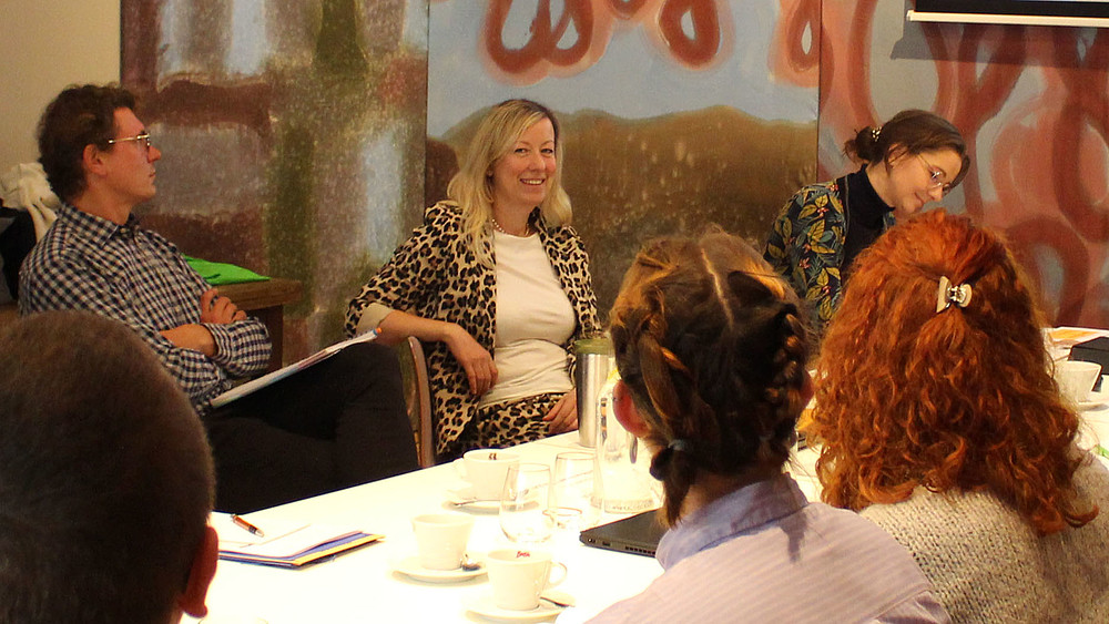 Die Prorektorin sitzt an einem Tisch zusammen mit Workshopteilnehmenden und lächelt in die Kamera.