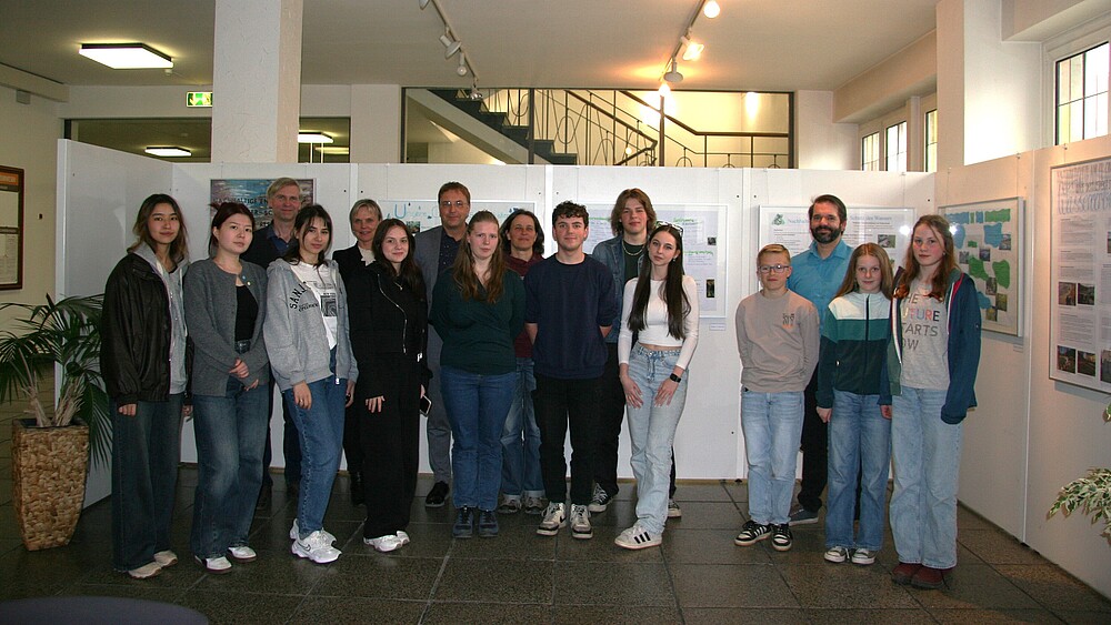 Schülerinnen und Schüler, Lehrende und Prof. Kroschel stehen vor einer Bilderausstellung nebeneinander.