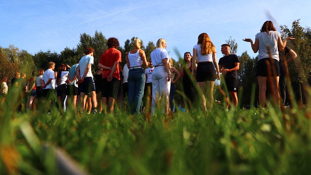 Studierende stehen auf einer Wiese und schauen sich an.