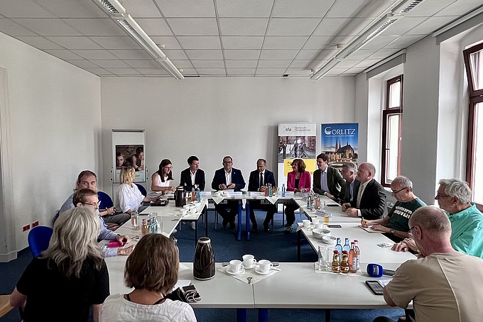 Die Gesellschafterinnen und Gesellschafter sitzen in einem Seminarraum an Tischen und besprechen sich.