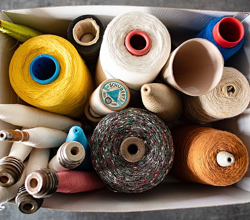 Ein Karton mit vielen Spindeln voller bundem Garn