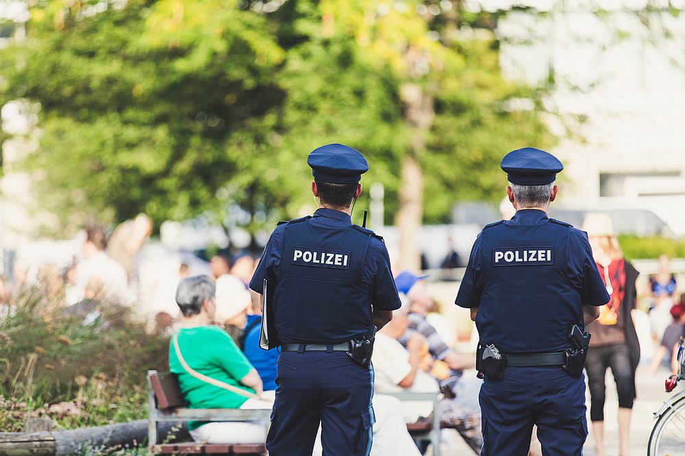 Zwei Polizisten stehen mit dem Rücken zur Kamera in einem Park mit Blick nach vorn gerichtet.