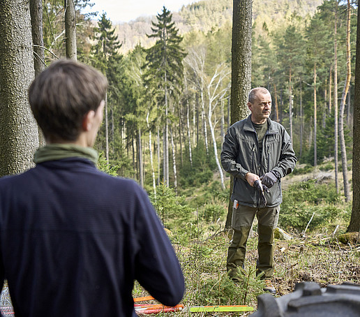 Ein Forstmitarbeiter erklärt Studierenden im Wald, wie man Bäume einplfanzt.