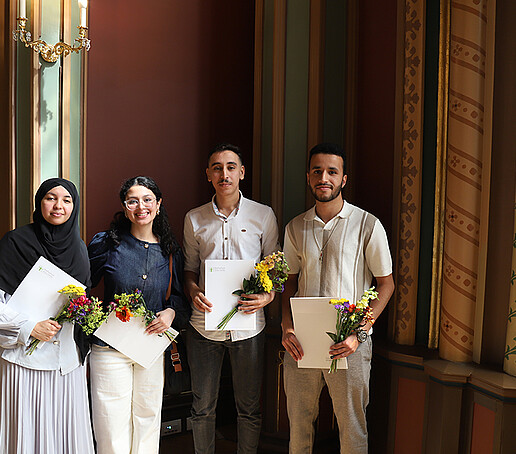 Eine Gruppe Absolventinnen und Absolventen stehen zum Gruppenbild nebeneinander und lächeln in die Kamera.