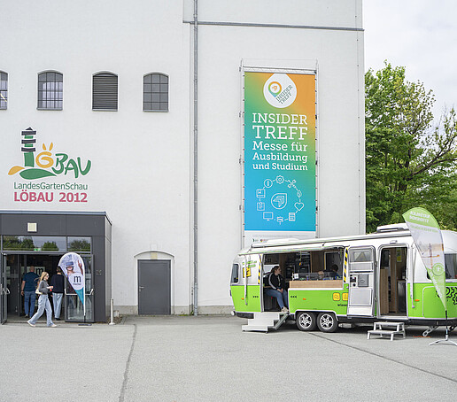 Auf dem Platz vor der Blumenhalle steht rechts neben dem Eingang der Airstream-Anhänger.