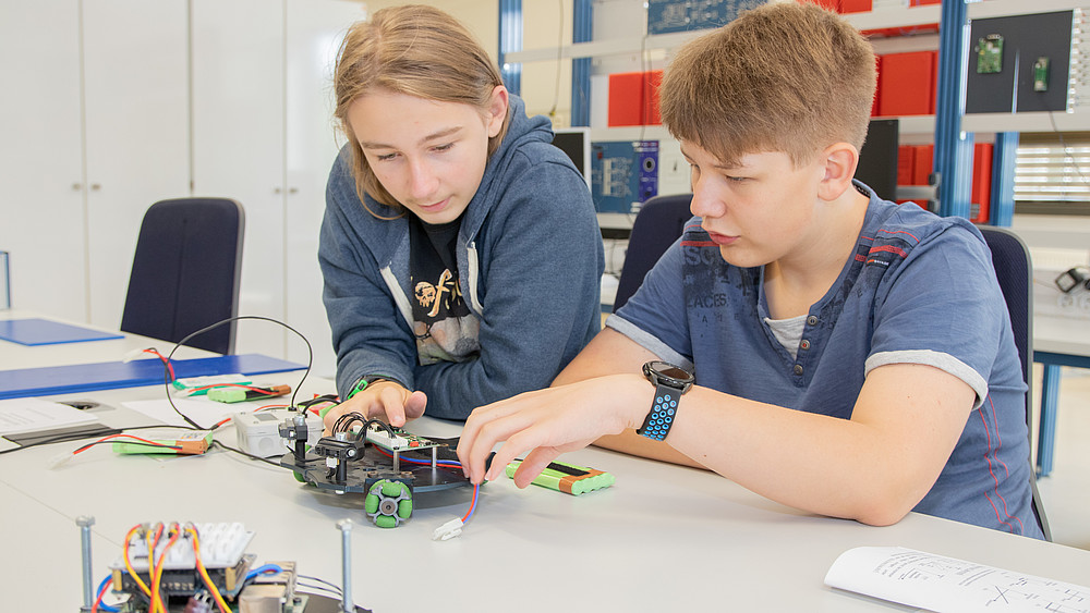 Zwei Schüler sitzen an einem Labortisch und befassen sich mit dem Aufbau eines Roboters.