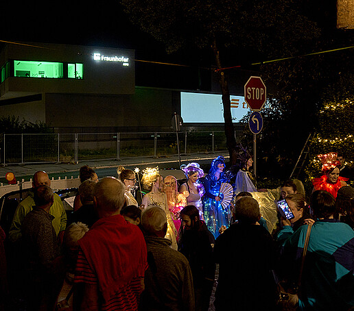 Besuchende stehen am Stadtring um eine Gruppe mit leuchtenden Kostümen.