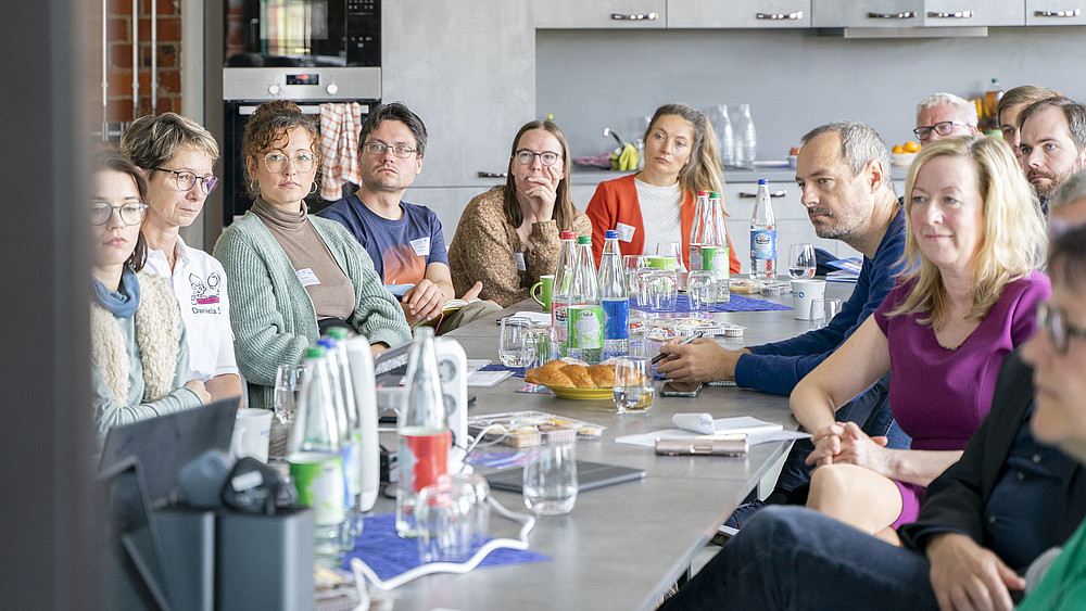 Hochschulmitarbeitende und Gäste sitzen im Celsiuz an einem langen Tisch und lauschen einem Vortrag.