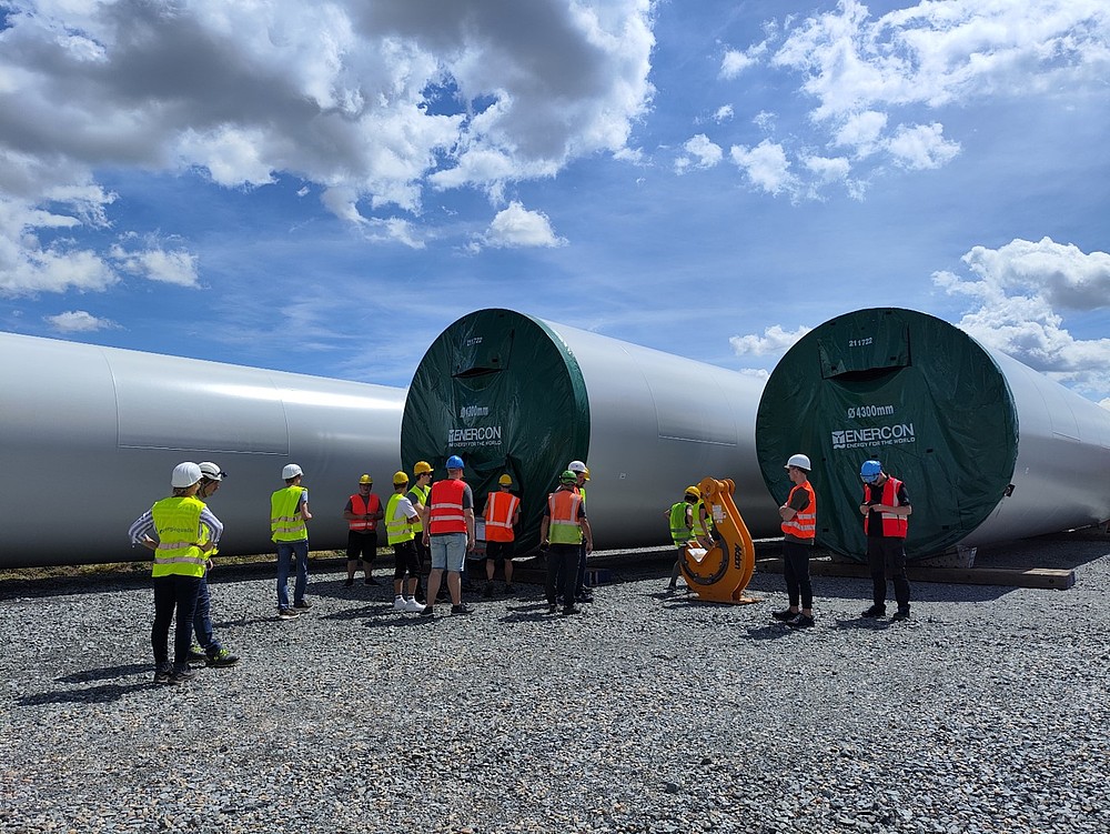 Eine Ansammlung von Menschen vor noch zu errichtetenden drei WIndrädern die auf einem Feld liegen