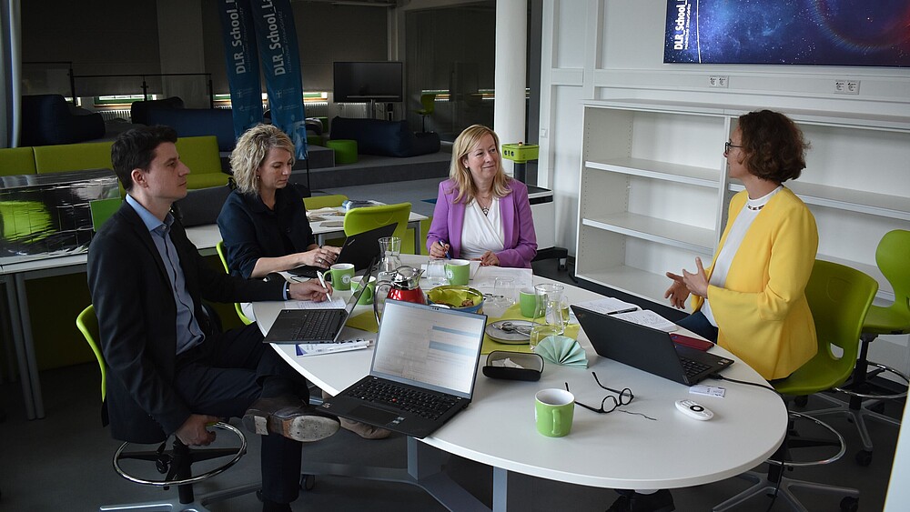 Die Prorektorin Sophia Keil, ihre Mitarbeiterin und zwei Vertretende von ZEUSS sitzen im DLR_School_Lab an einem Tisch und diskutieren.