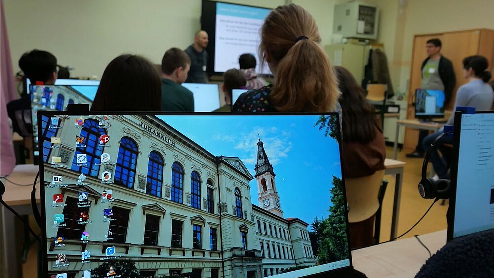Ein voll besetztes Klassenzimmer. Die Schülerinnen und Schüler sitzen vor Bildschirmen, auf dem das CWG abgebildet ist.