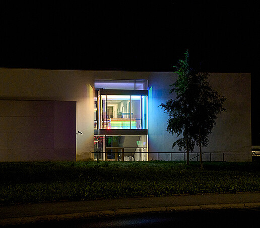 Das Fenster eines Hochschulgebäudes leuchtet in Regenbogenfarben.