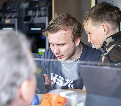 Ein Junge schaut einer Studentischen Hilfskraft im Airstream-Anhänger über die Schulter.