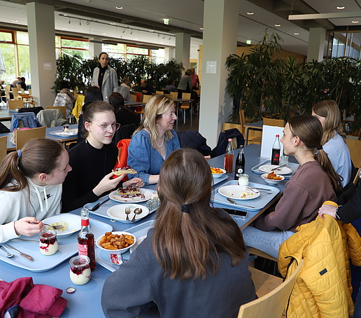 Die Prorektorin sitzt mit Schülerinnen am gedeckten Tisch in der Mensa und unterhält sich mit ihnen.