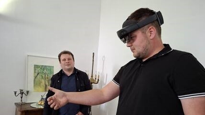 Dr. Belov schaut einem Mann beim Ausprobieren einer KI-Brille zu.