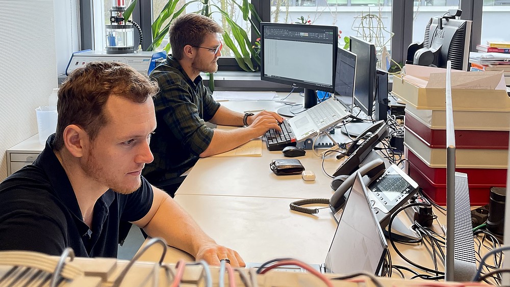Jan-Hendrik Smith und Karl Jacobie sitzen an ihren Rechnern am Schreibtisch und arbeiten.