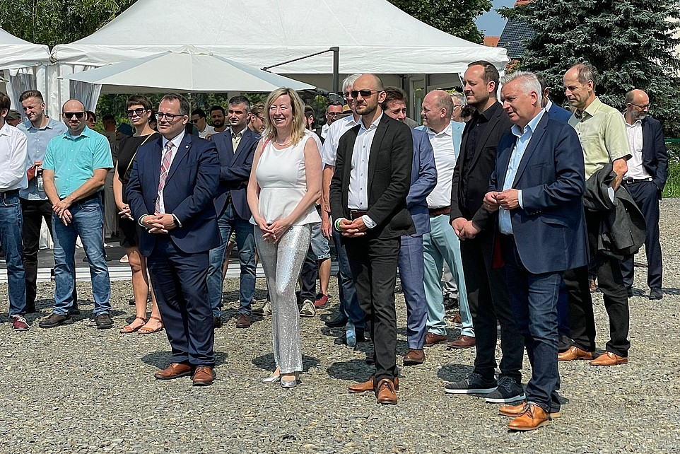 Die Hochschulleitung und Gäste stehen im Freien vor einem Pavillon und lauschen jemandem, der im Bild nicht zu sehen ist.