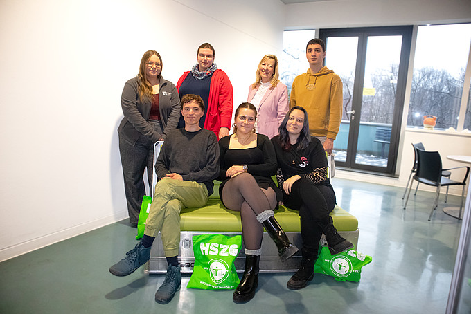 Studierende und die Prorektorin stehen und sitzen als Gruppe hintereinander und lächeln in die Kamera.