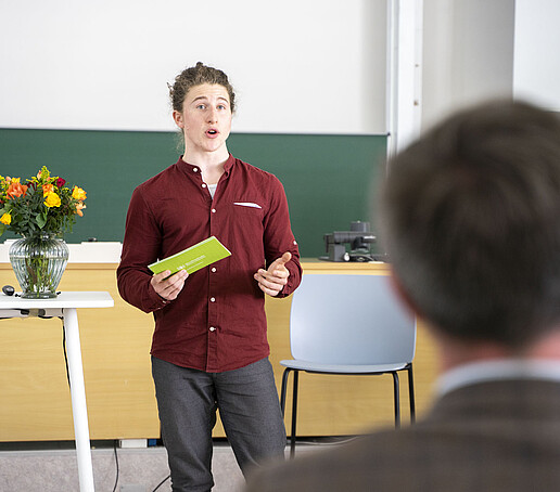 Der Moderator hält eine Karte und eröffnet die Veranstaltung.