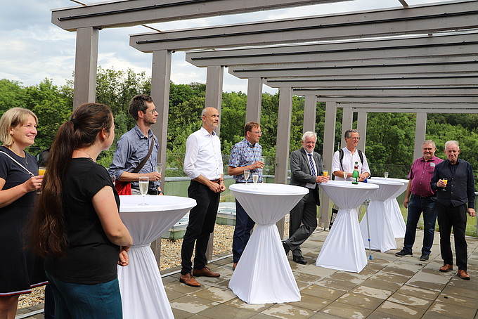 Senatorinnen und Senatoren stehen unter einer Überdachung und halten Gläser in die Höhe zum Anstoßen.