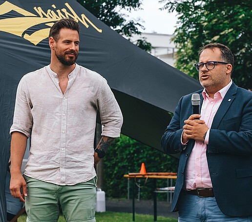 Der Rektor spricht in sein Handmikro, Philipp Knebel steht daneben. 