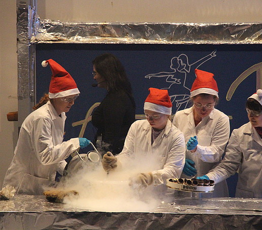 Vier Chemiker mit Weihnachtsmützen führen auf der Bühne ein dampfendes Experiment durch.