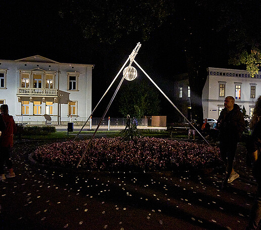 Eine Diskokugel hängt an einer Röhrenaufhängung und wird angeleuchtet. Besucher gehen daran vorbei.