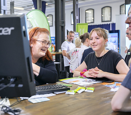 Besucherinnen informieren sich an einem Tisch bei einer Mitarbeiterin.