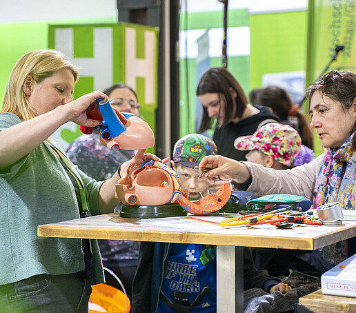 Besucherinnen probieren Ausstellungsstücke am Pflegewissenschafts-Stand aus.