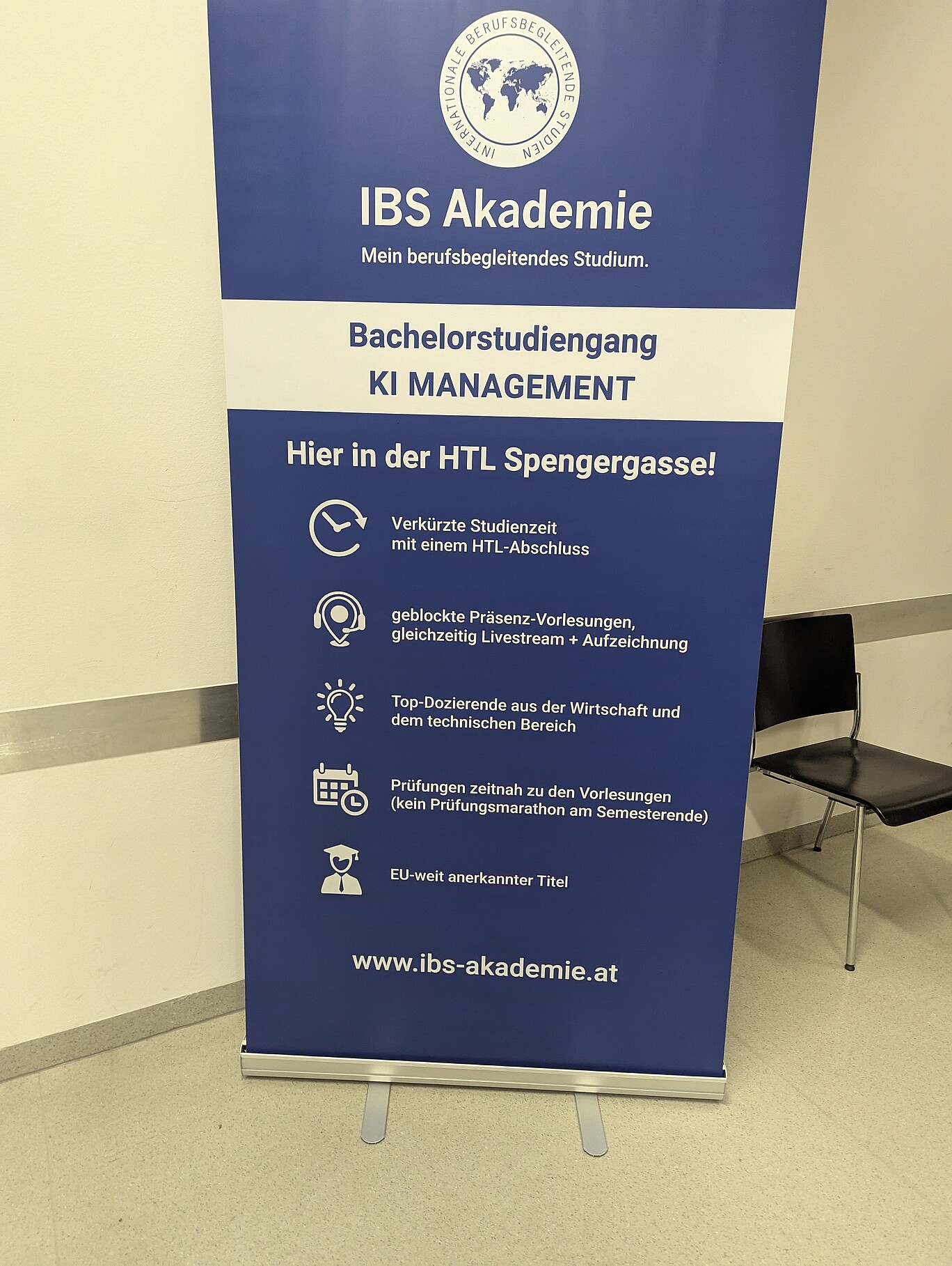 Blaues Roll-Up der IBS Akademie mit Informationen zum berufsbegleitenden Bachelorstudiengang „KI MANAGEMENT“ an der HTL Spengergasse. Auf dem Plakat sind Vorteile wie verkürzte Studienzeit, geblockte Präsenzvorlesungen mit Livestream, Top-Dozierende und EU-weit anerkannter Titel aufgelistet. Darunter befindet sich die Webadresse www.ibs-akademie.at.
