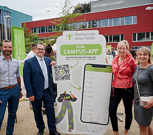 Herr Rönisch, der Rektor, die Prorektorin und Frau Korb vor dem Campus-App-Aufsteller.