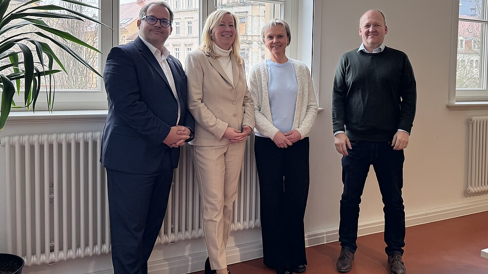 Das Rektorat steht am Fenster des Senatssaals und lächelt in die Kamera.