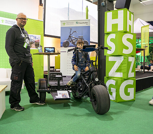 Ein Junge sitzt auf dem Wasserstoff-Roller, ein Mitarbeiter steht daneben.