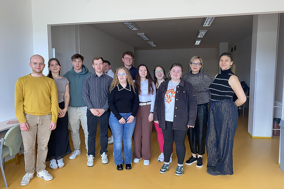 Studierende und Lehrende stehen nebeneinander und lächeln in die Kamera.