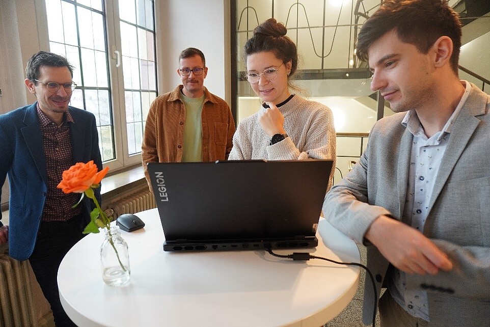 SCO-TTi-Mitarbeitende beraten sich an einem Stehtisch mit aufgeklappten Laptop.
