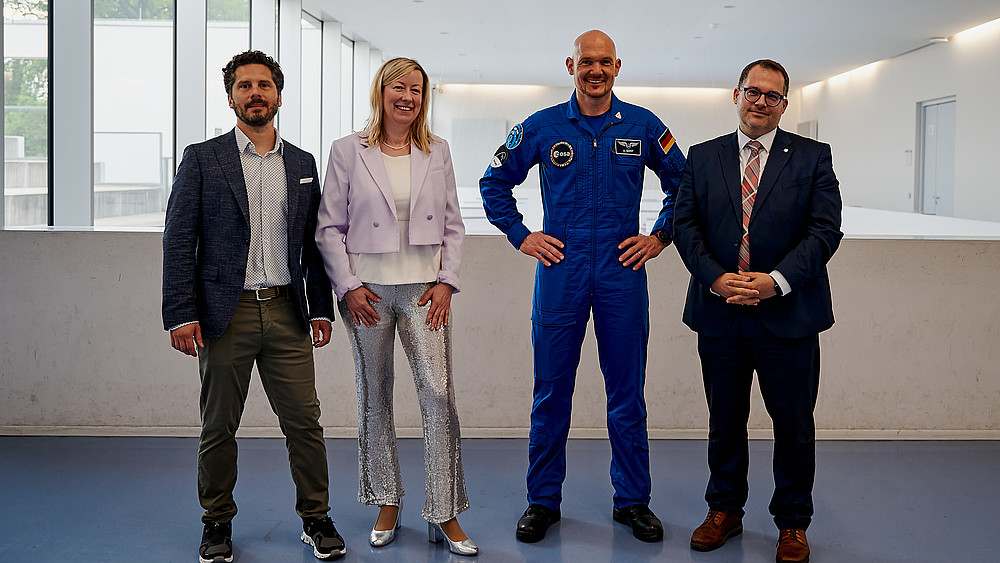 Christian Tiller, die Prorektorin, Alexander Gerst und der Rektor stehen im ersten Stock von Haus eins und lächeln in die Kamera.