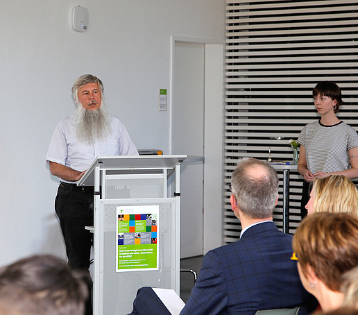 Ein Vortragender mit Vollbart steht am Rednerpult.