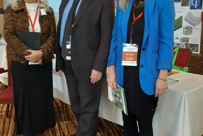 Teilnehmende vor einem Tisch mit Roll-ups lächeln in die Kamera.