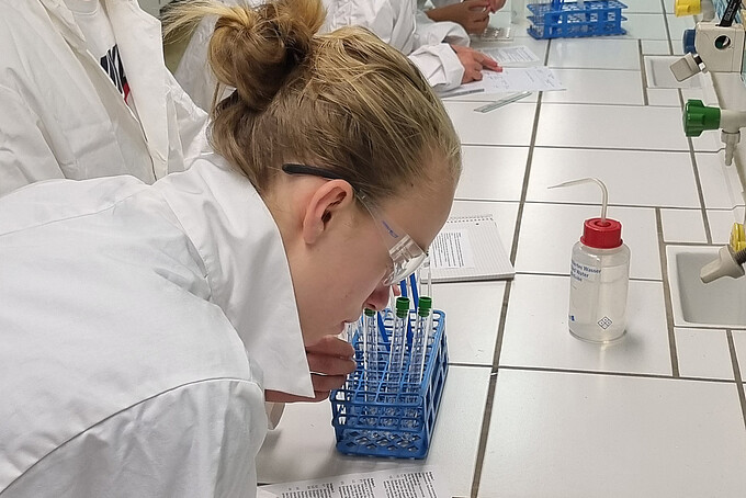 Schüler und Schülerinnen in weißen Kitteln stehen im Labor und experimentieren.