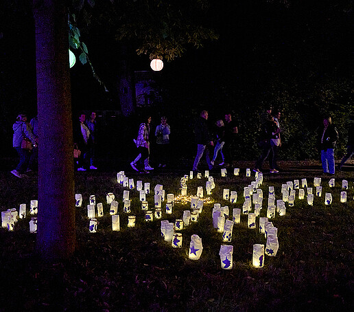 Kerzen in Backpapiertüten formen das Muster eines Schmetterlings auf einer Wiese. 
