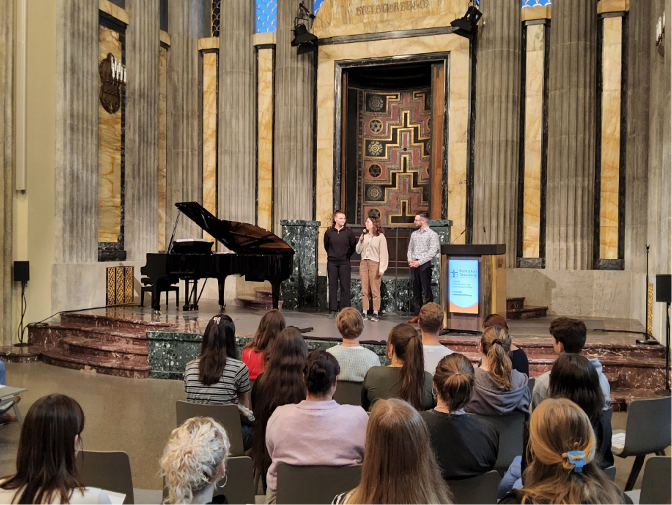 Elsa Richter und Viktoria Budde vom Fachschaftsrat sowie Moderator Lennart Höhne auf der Bühne