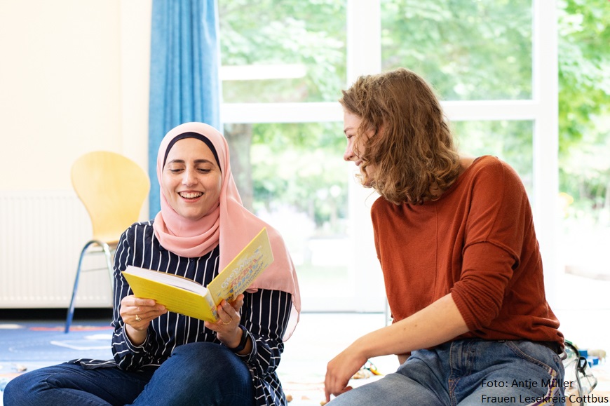 Zwei Frauen sitzen lachend auf dem Fußboden.