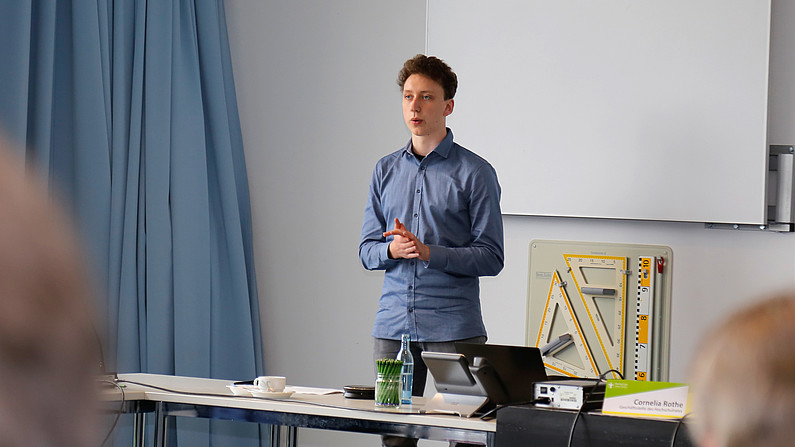 Deutschlandstipendiat Lucas Wünsche bei einem ehrenamtlichen Einsatz für den StuRa. Er steht im Seminarraum vor Publikum und hält eine Rede.